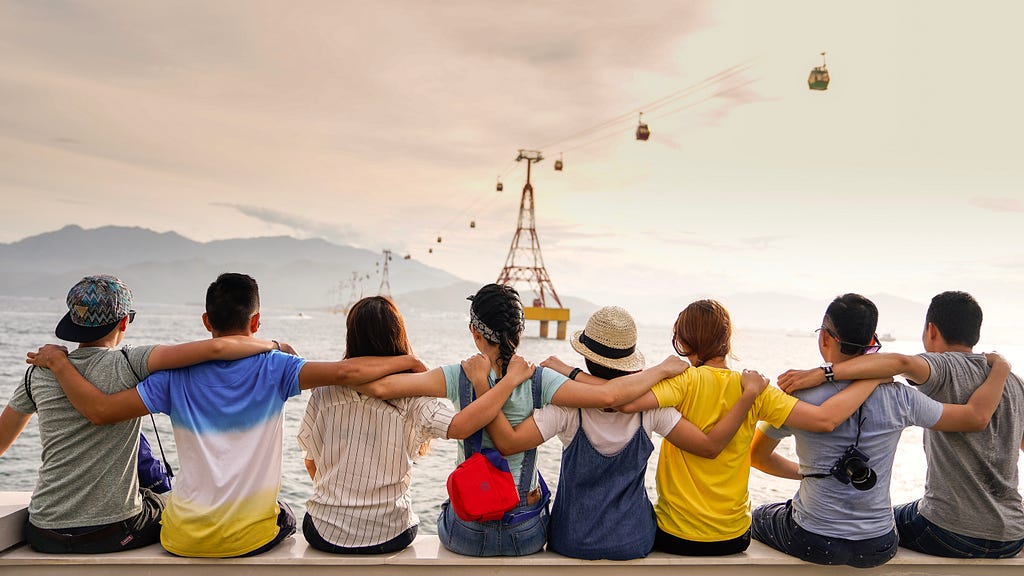 A group of people sitting on a dock with their arms around each other looking out at a body of water