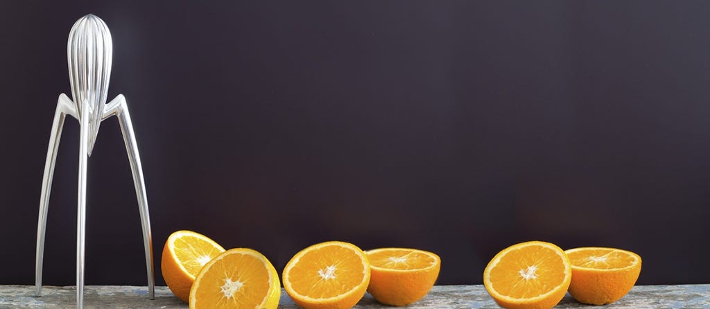 Foto do renomado espremedor de frutas de Philippe Starck, cercado de laranjas cortadas pela metade, prontas para serem espremidas.