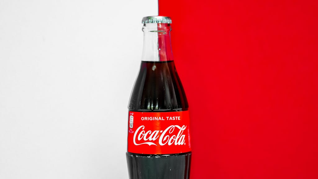 An image of a glass Coca-Cola bottle in front of a red-and-white background.