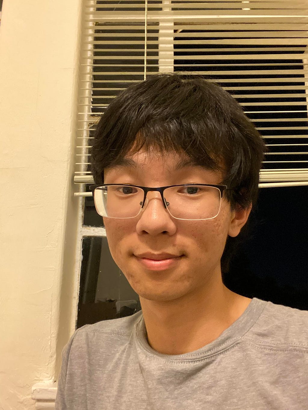 A close-up of a smiling person with black hair, wearing glasses and a T-shirt.