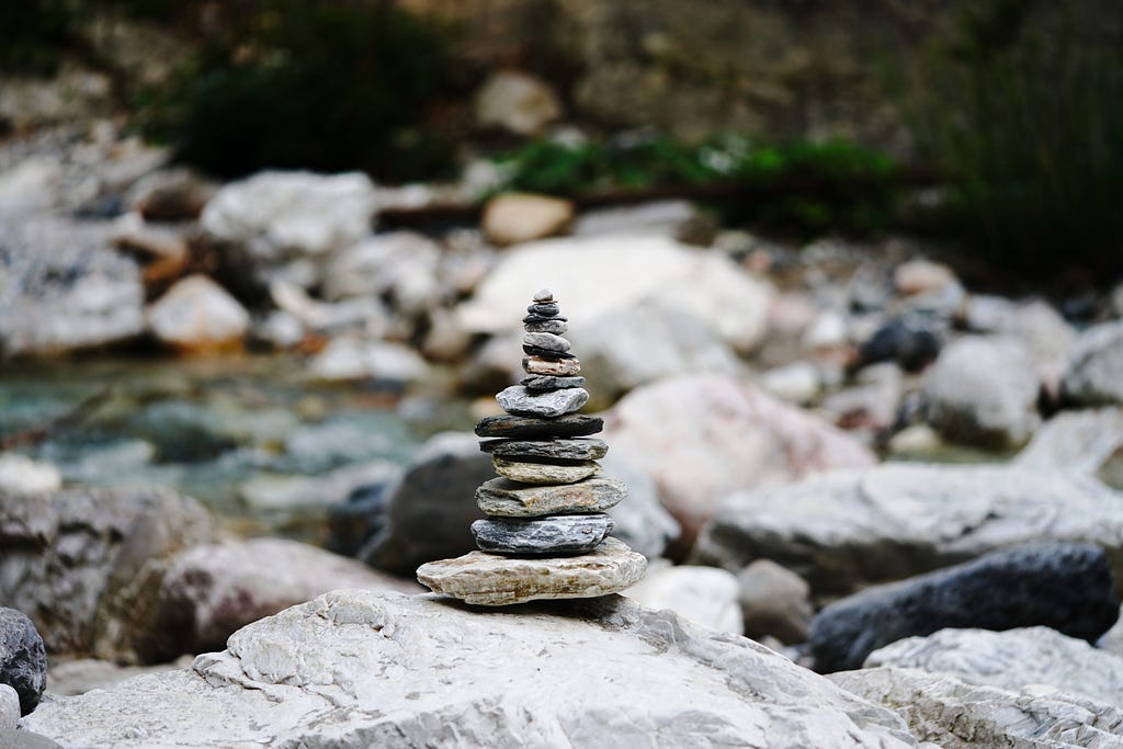 A cairn of stone in foreground with rocky stream in blurry background