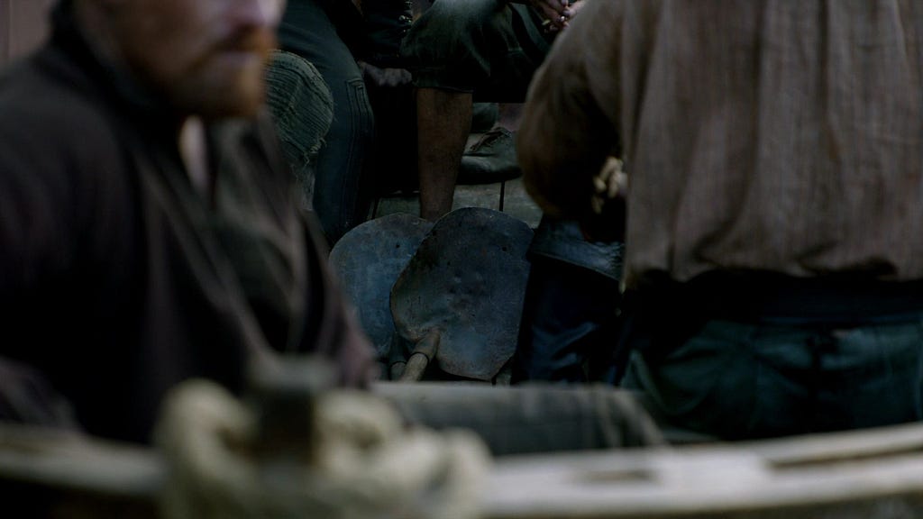 Two shovels lie in the bottom of a boat behind Flint, out of focus in the foreground.