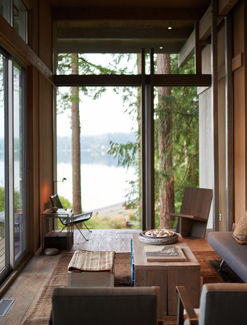 Living Room, Coffee Tables, Chair, Medium Hardwood Floor, Rug Floor, Table Lighting, and Sofa The living room’s large wall of glass frames a view of the adjoining grassy field and Puget Sound, visually blending indoors and outdoors.&nbsp;