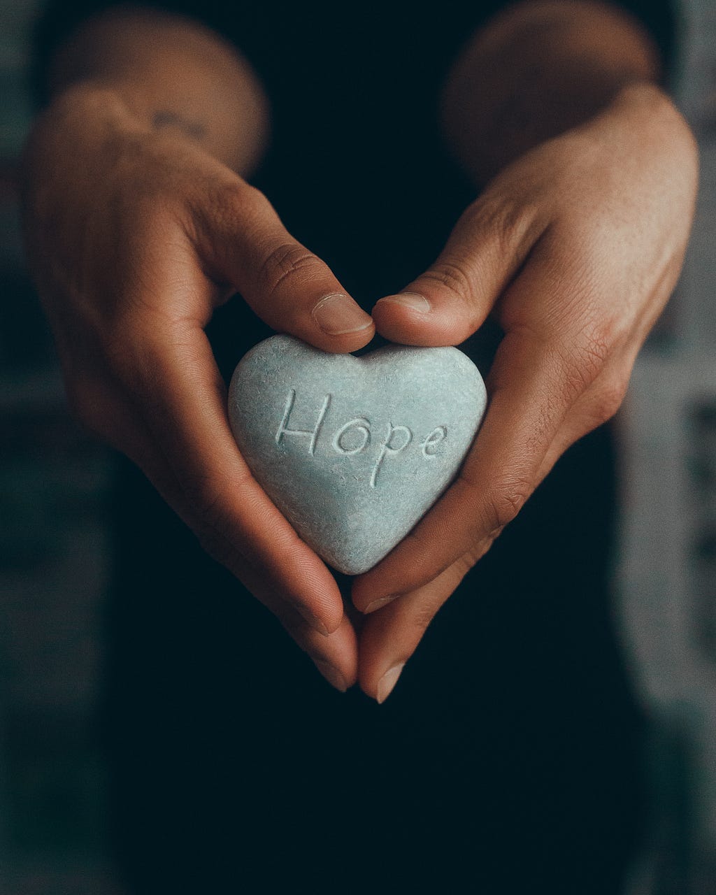 hands hold heart shaped stone with word hope