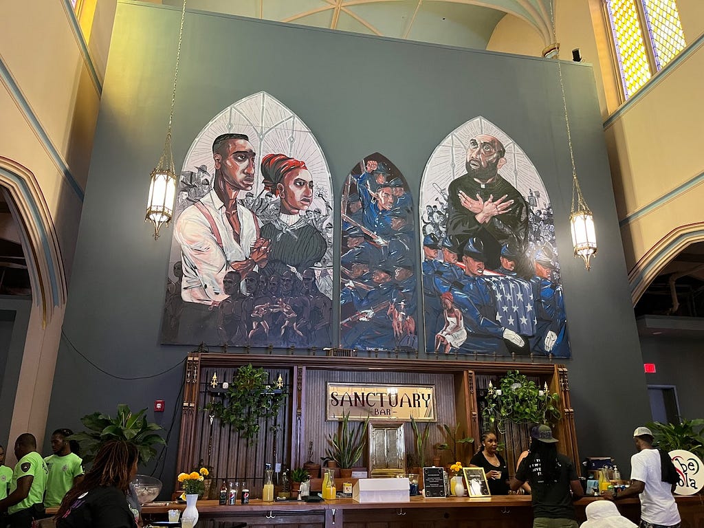 Mural of stained glass featuring Black woman, man and minister over a bar.