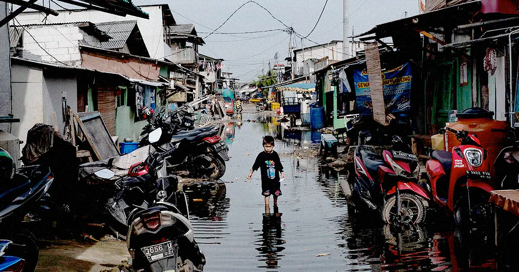 A boy walks down a flooded shanty town street in Jakarta