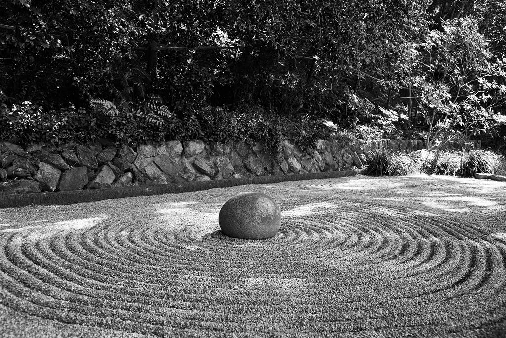 A boulder in the middle of a raked Japanese gravel garden.