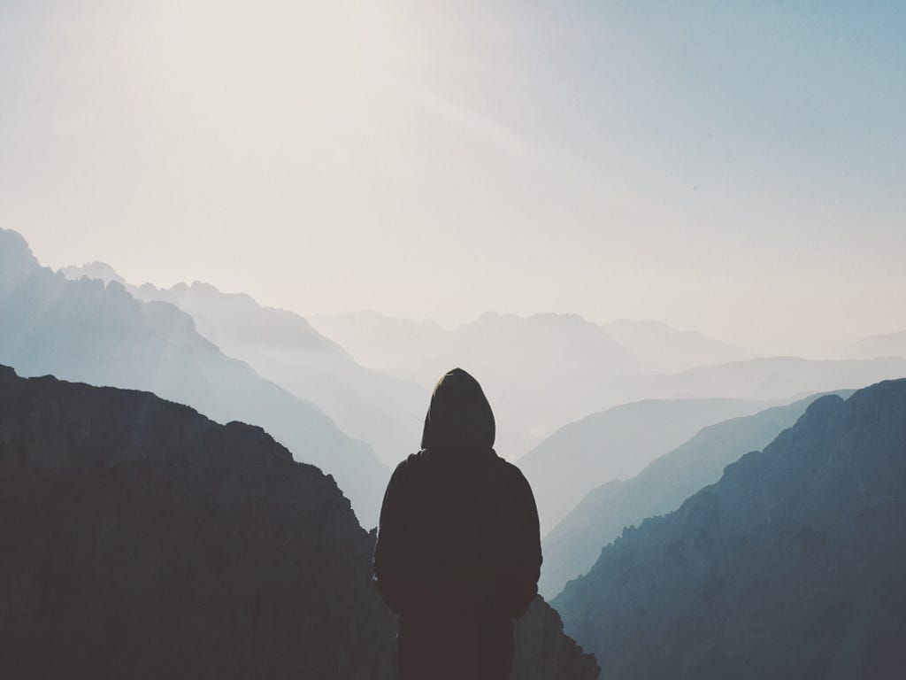 Person standing in front of a mountain, confronting and naming their pain to achieve self-compassion