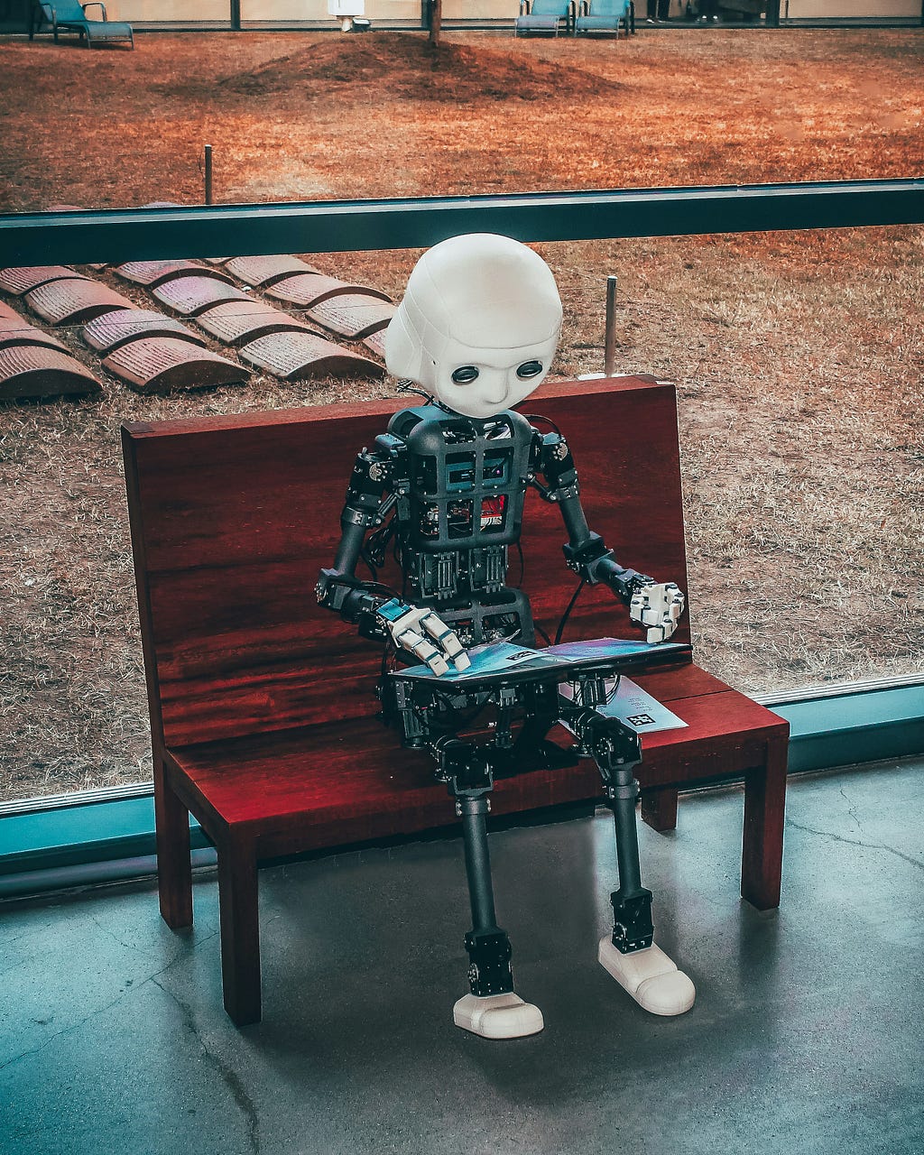 Humanoid robot sitting on a bench and typing on a computer keyboard.