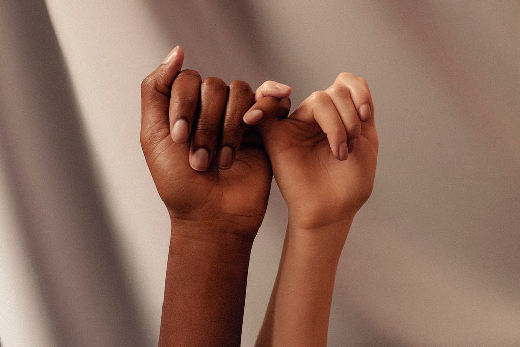 Two hands, mixed race with pinkies connected in a lite. Various gradient shade of brown as the background.