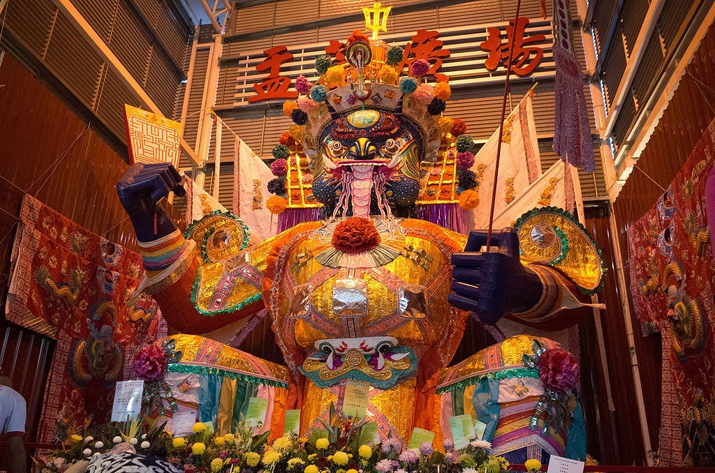 A vibrant ‘Dai She Ye’ paper effigy standing amidst festive decorations at the Hungry Ghost Festival in Bukit Mertajam, Penang, Malaysia — August 2018, featuring intricate patterns and colorful adornments symbolizing prosperity and good fortune.