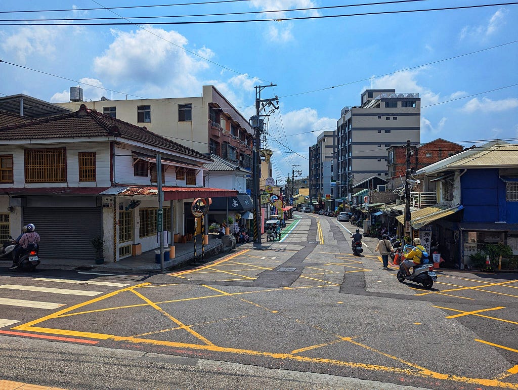 The quiet street outside Houli Railway Station. There are some bike rental shops and scooters riding by.