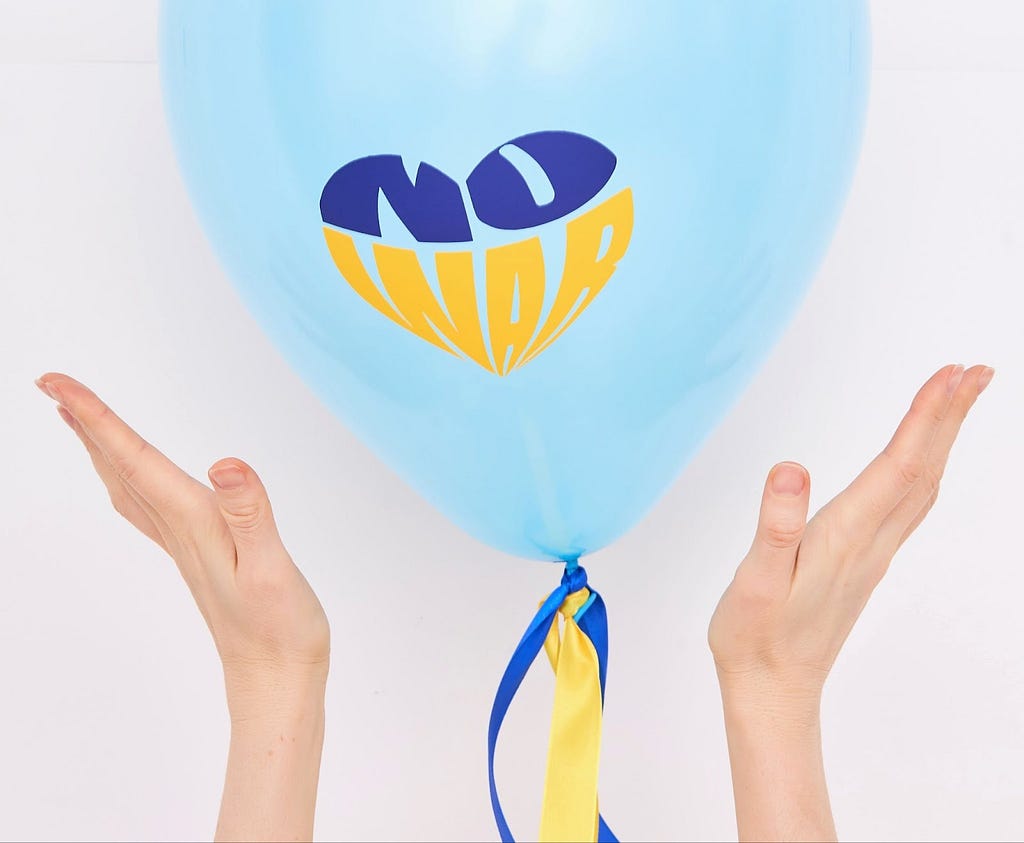 two hands showcasing a blue balloon with a sign that says ‘no war’