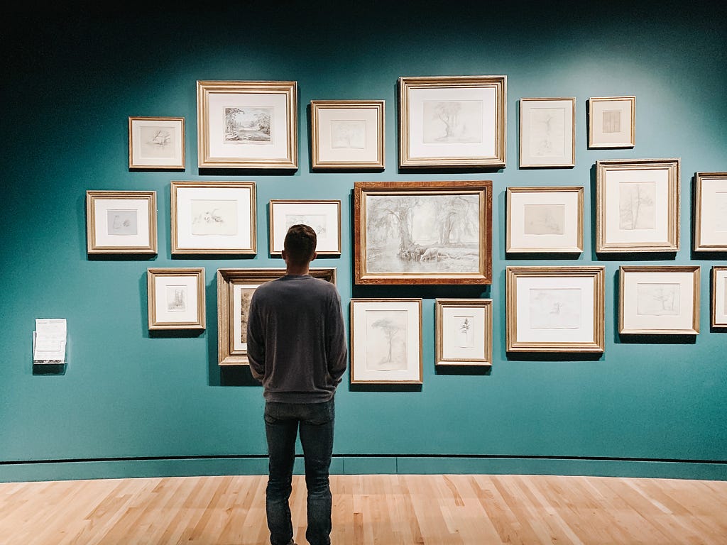 Person looking at wall crowded with framed drawings