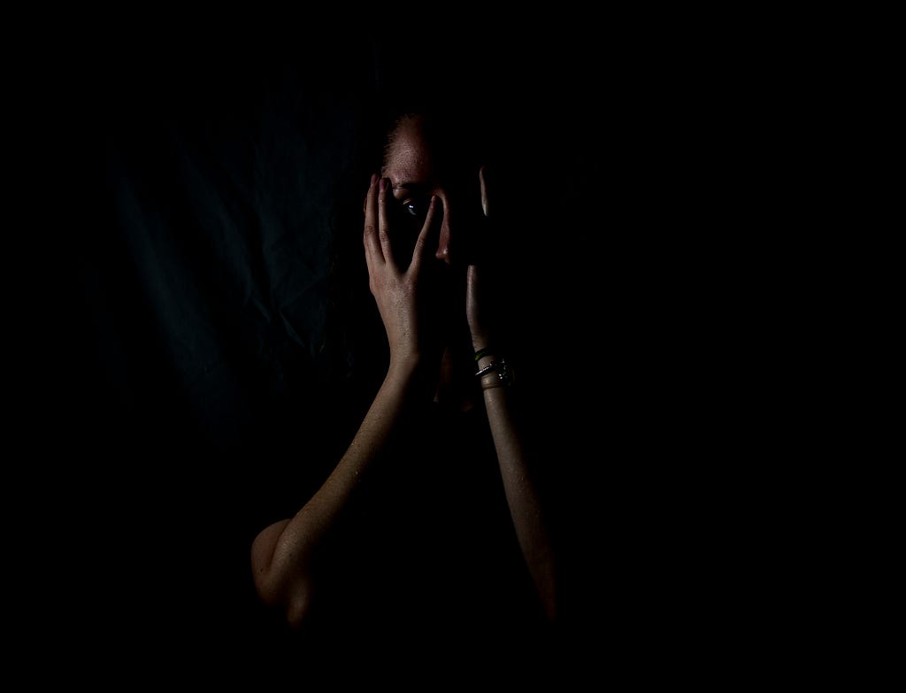 A dark picture of a person covering their face with their two hands; face in hands.