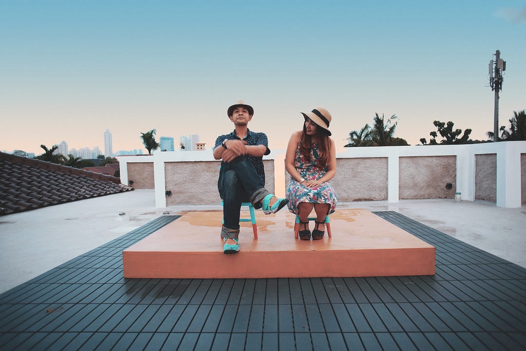A man and woman sit on a roof top at dusk
