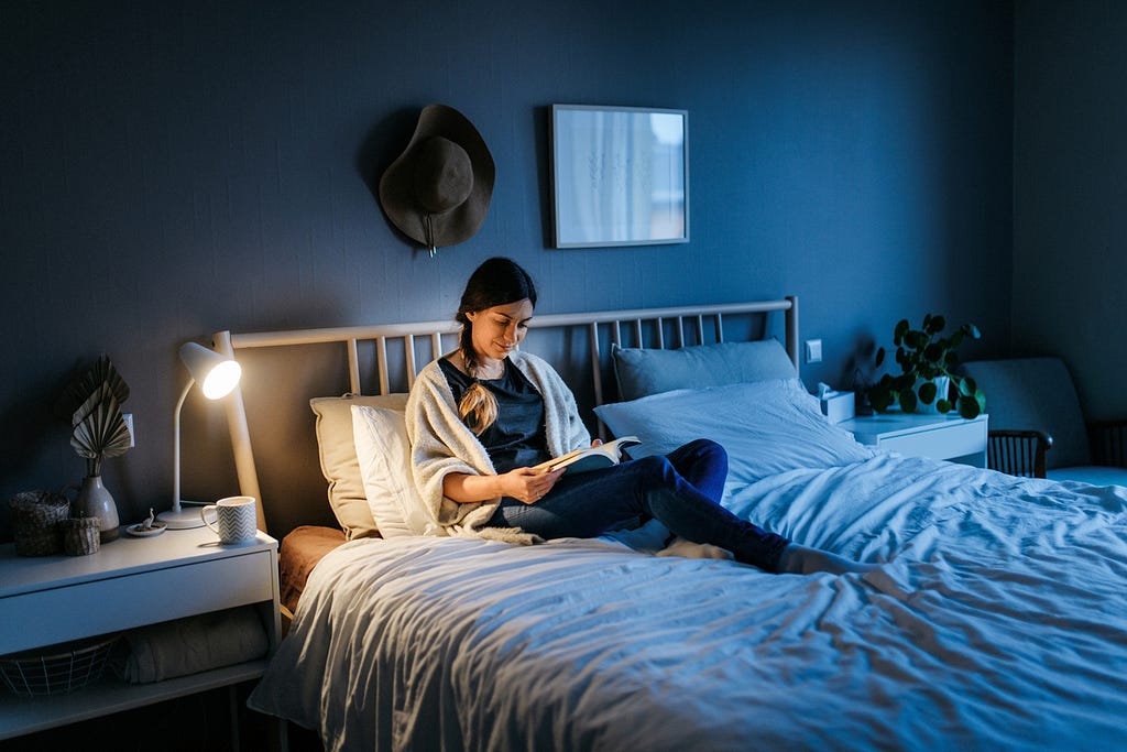 Woman in bed reading a book in very dim lighting.