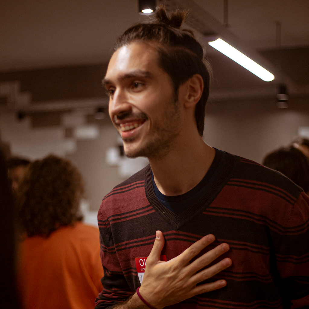 The smiling person in the picture has a hand over their heart and their hair in a bun.