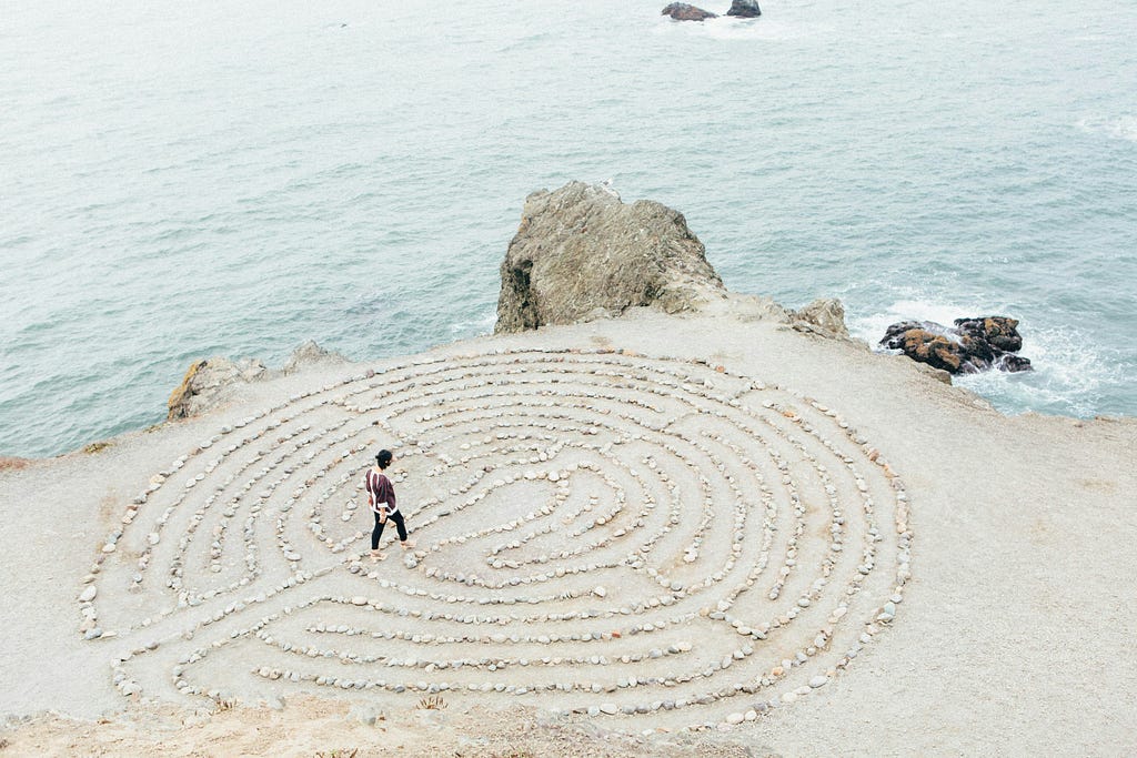 Person walking a sand labyrinth near the sea