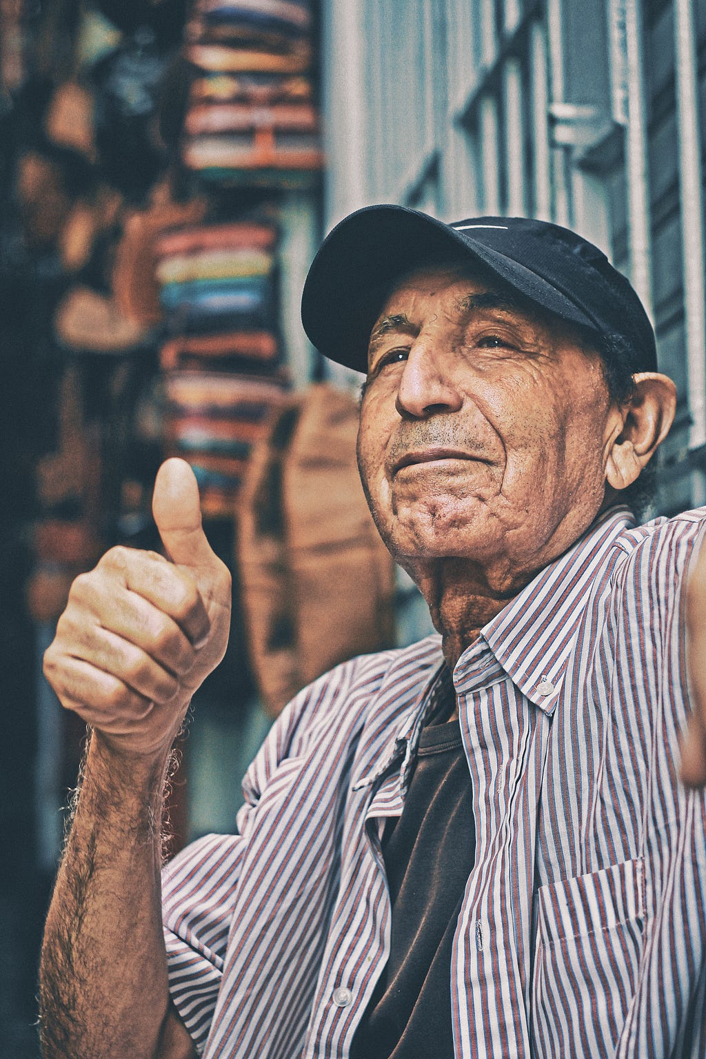 An older man wearing a cap making a thumbs up gesture