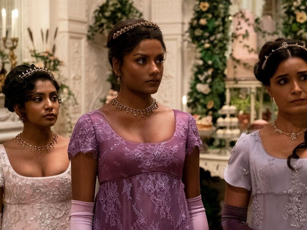 An image shows the Sharma family from Bridgerton Season 2. They are period gowns with tiaras and necklesses to match.