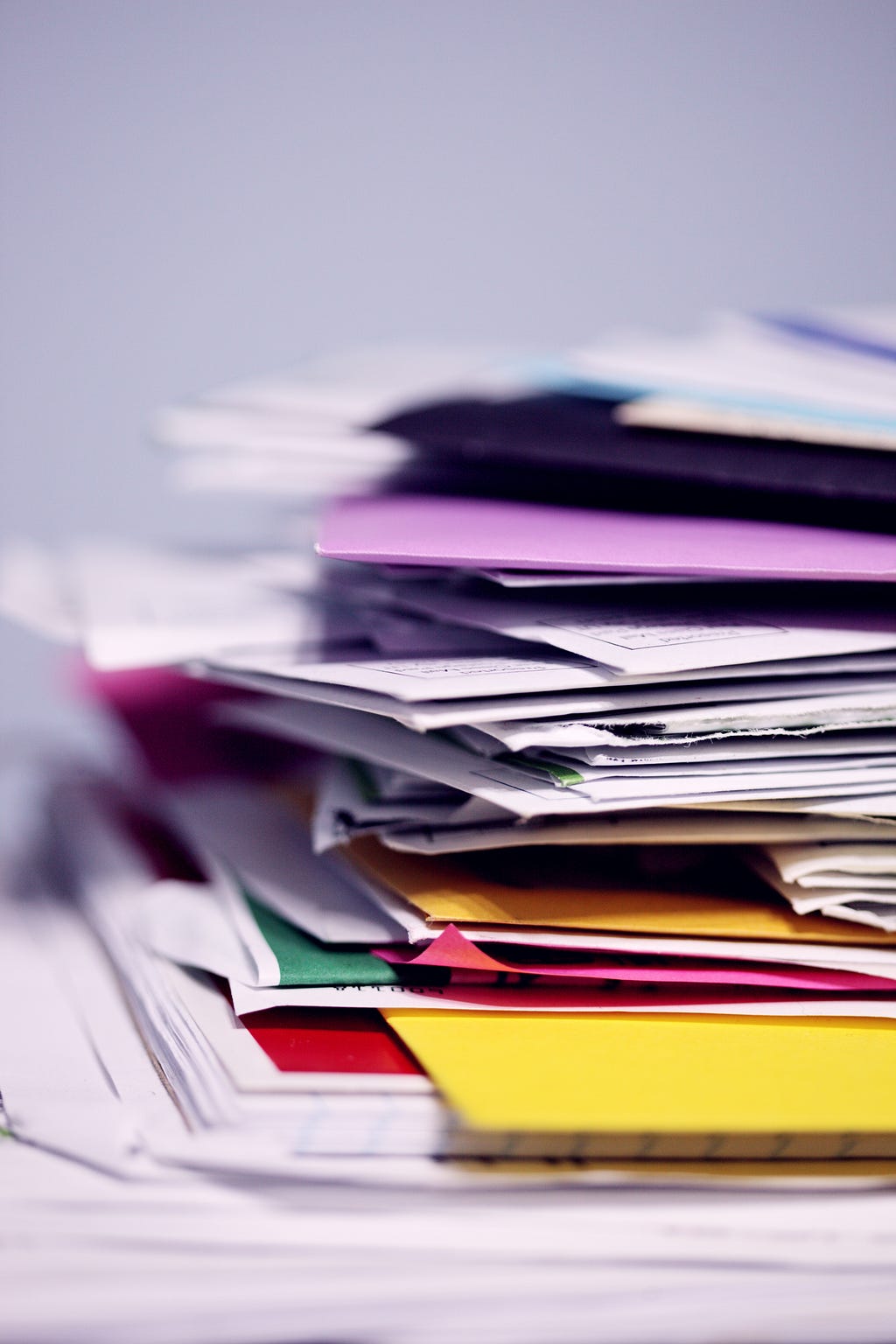 stacked papers and file folders in different colours. All askew. zoomed in view. Some background blur.