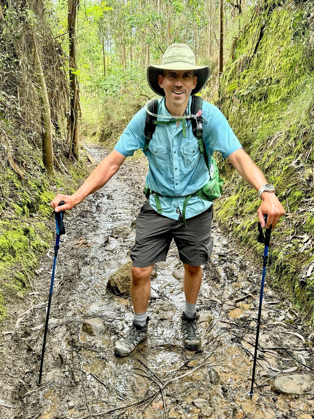 The author with two hiking sticks, pausing for a rest on steep muddy trail.