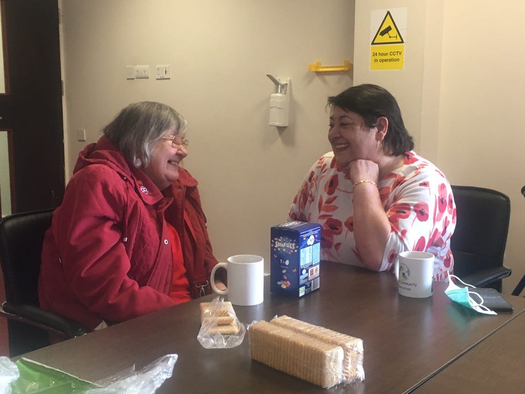 Two ladies laughing at a table, with a Smarties Easter egg, two mugs and custard creams on the tale