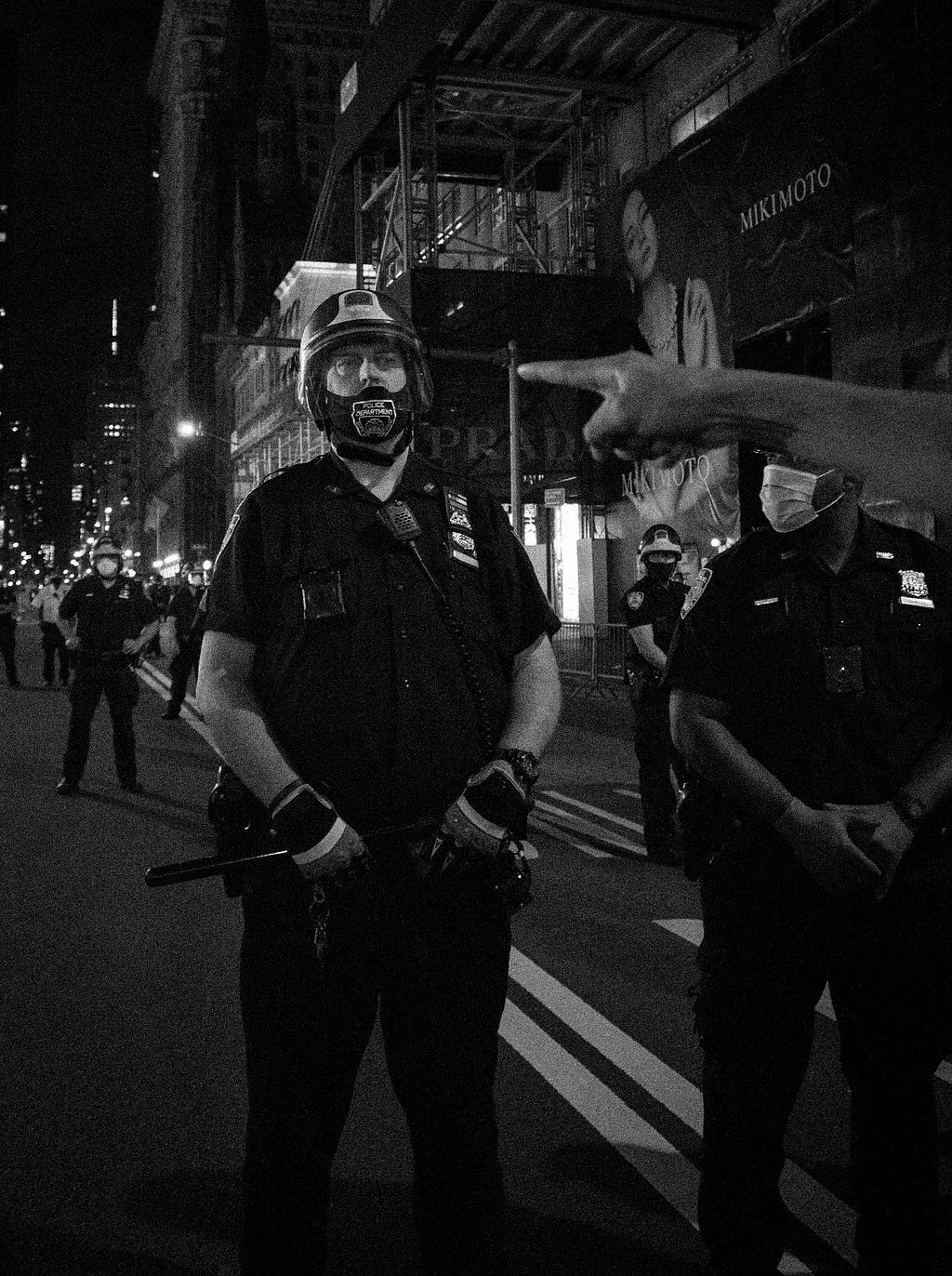 A hand points towards the head of an NYPD police officer during BLM protests