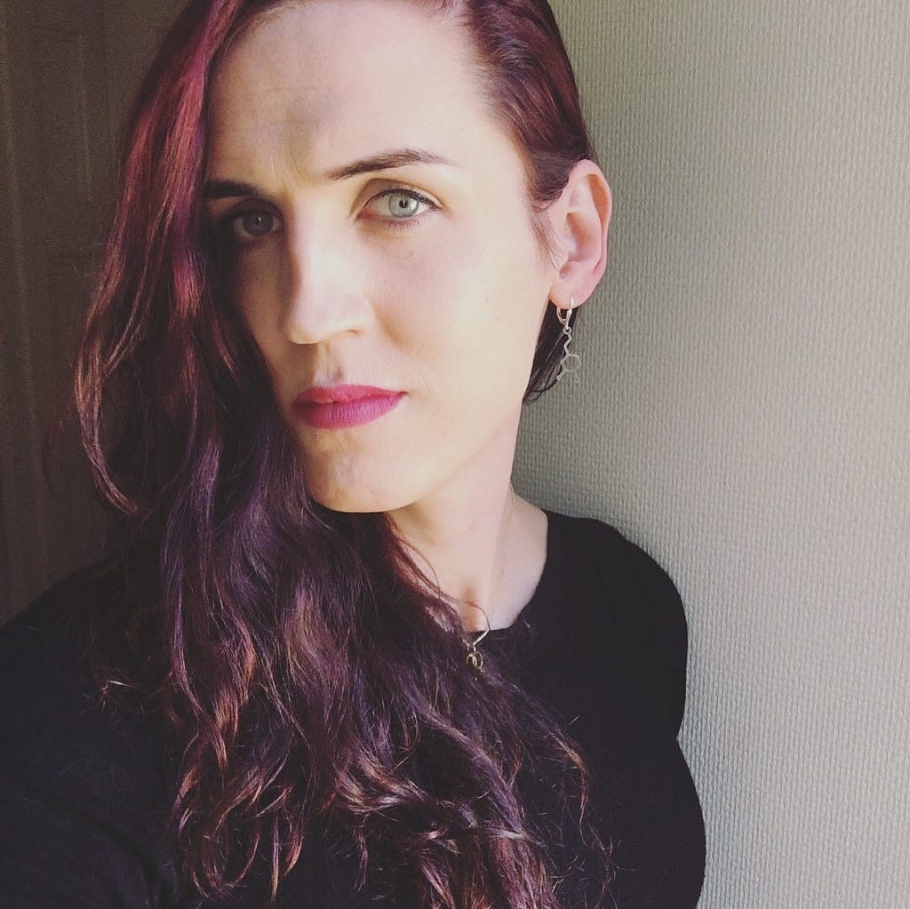 Selfie with dramatic lightning, pink lipstick, looking into the camera.