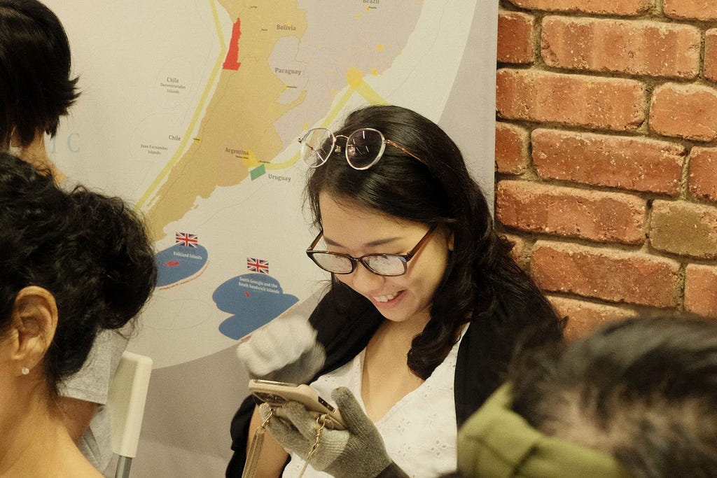 A woman wearing the smeared glasses and gloves smiling at her smartphone