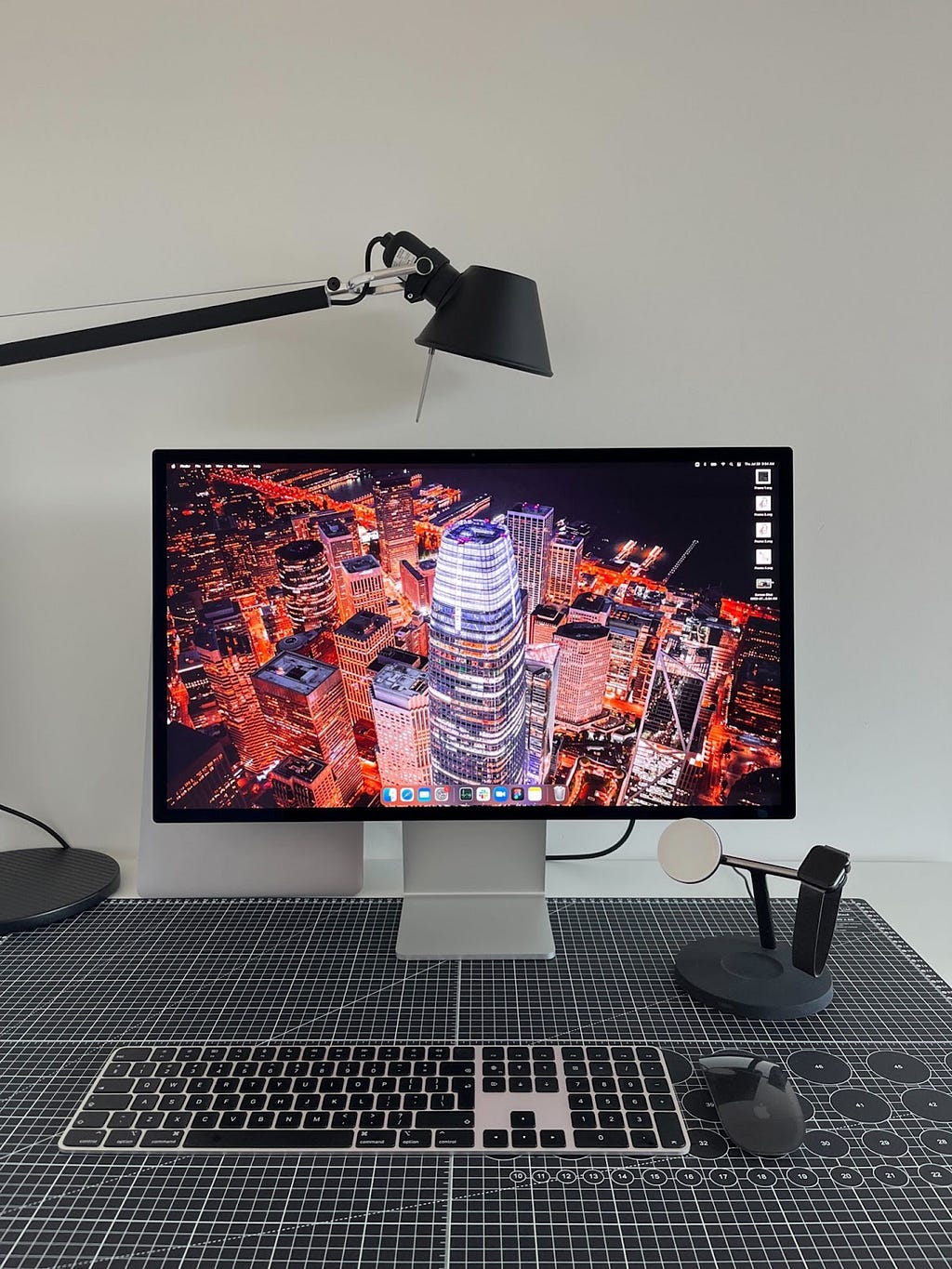 Image of a desk setup with a monitor, lamp and apple charging station.