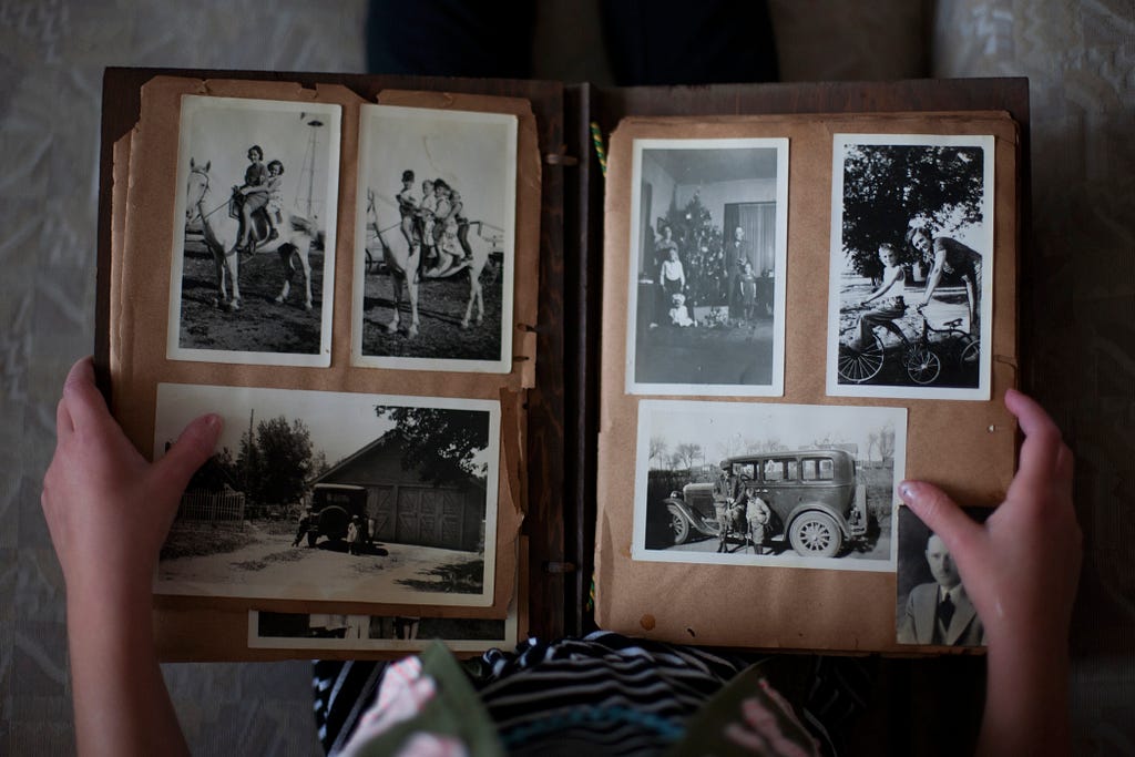 An image shows a photo album with 6 black and white photos in it. Two hands hold the album.