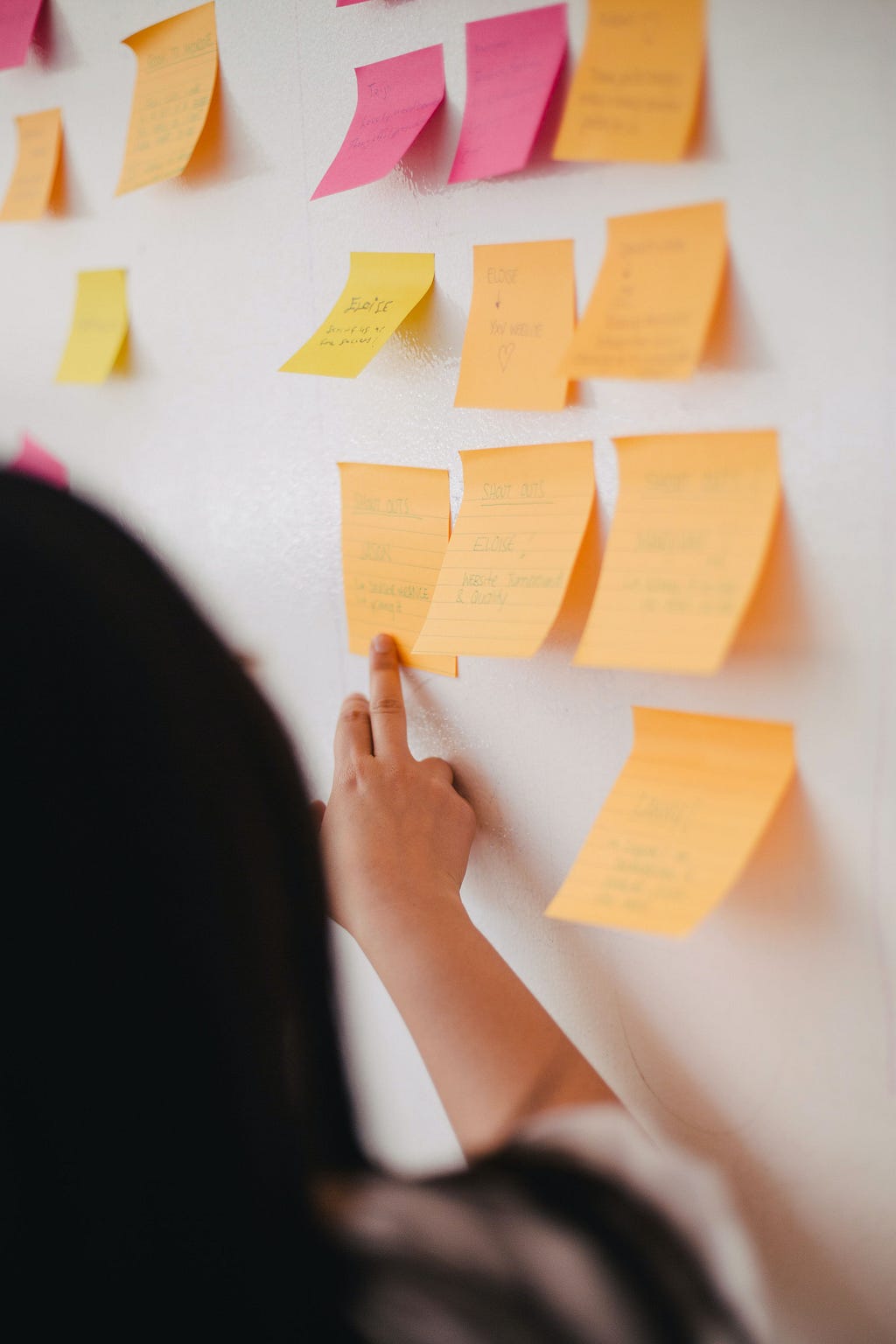 Uma mulher apontando para um quadro de post-its de cores laranja e rosa.