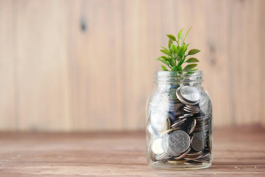 A glass jar with coins and a plant growing out of it