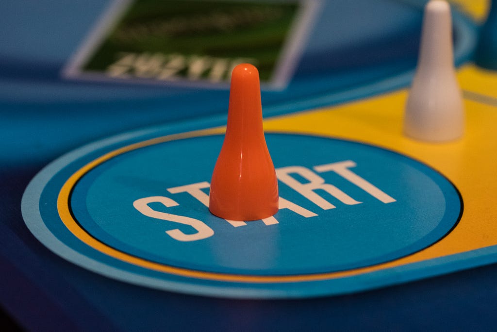 Imagem de um jogo de tabuleiro, com o foco em um pino laranja em específico. Abaixo dele, um círculo onde se lê “start”