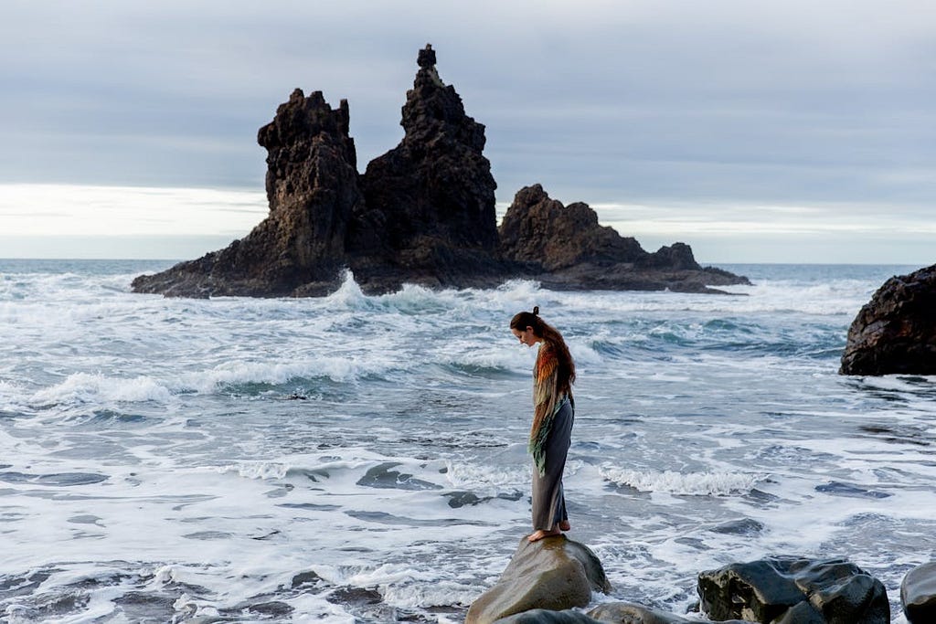 Lonely woman standsing on rocky coast.