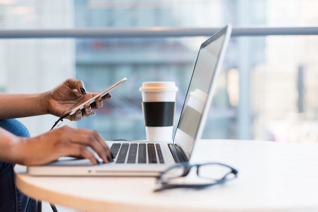 A person holding a phone on the left hand and resting the right on a laptop.