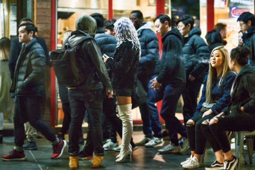 A young woman looking at her phone, standing still in the middle of a crowd.