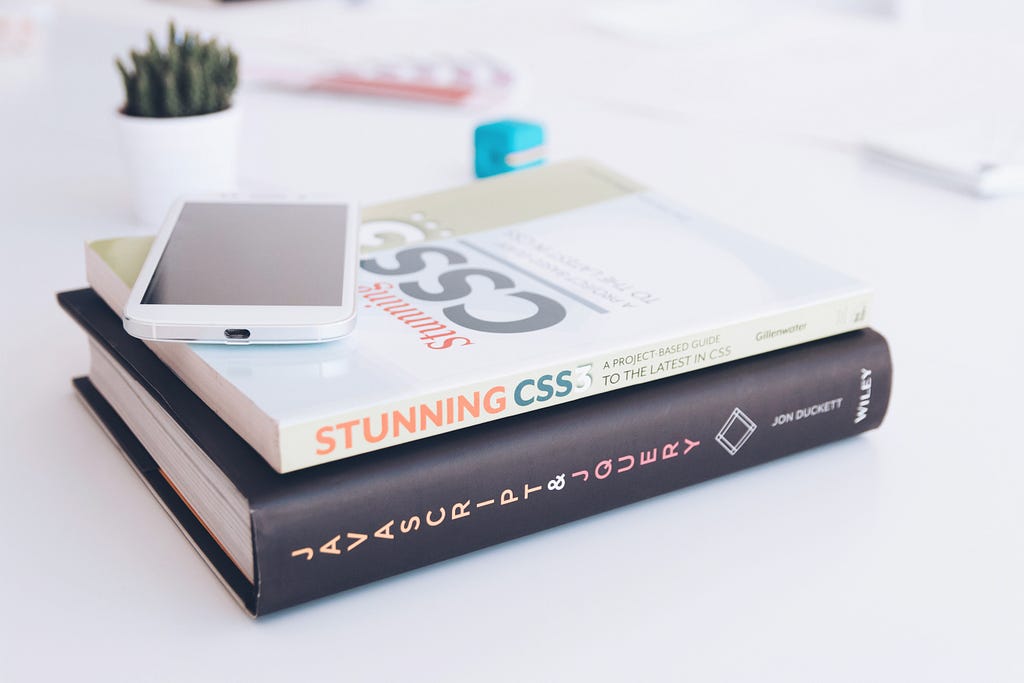 A stack of engineering books, a phone, and a plant. The top book is titled  “Stunning CSS”.