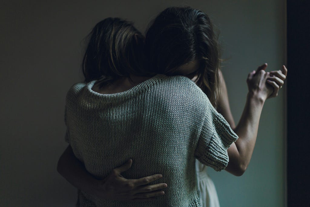 Two women hugging and supporting each other.