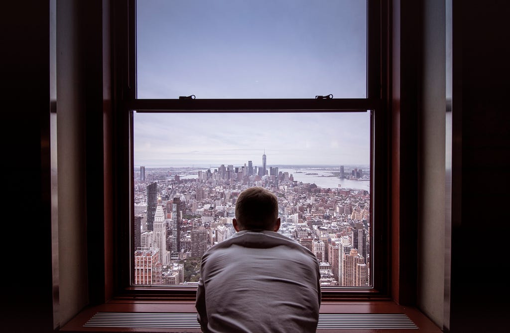 Man staring out the window, down at a metropolis.