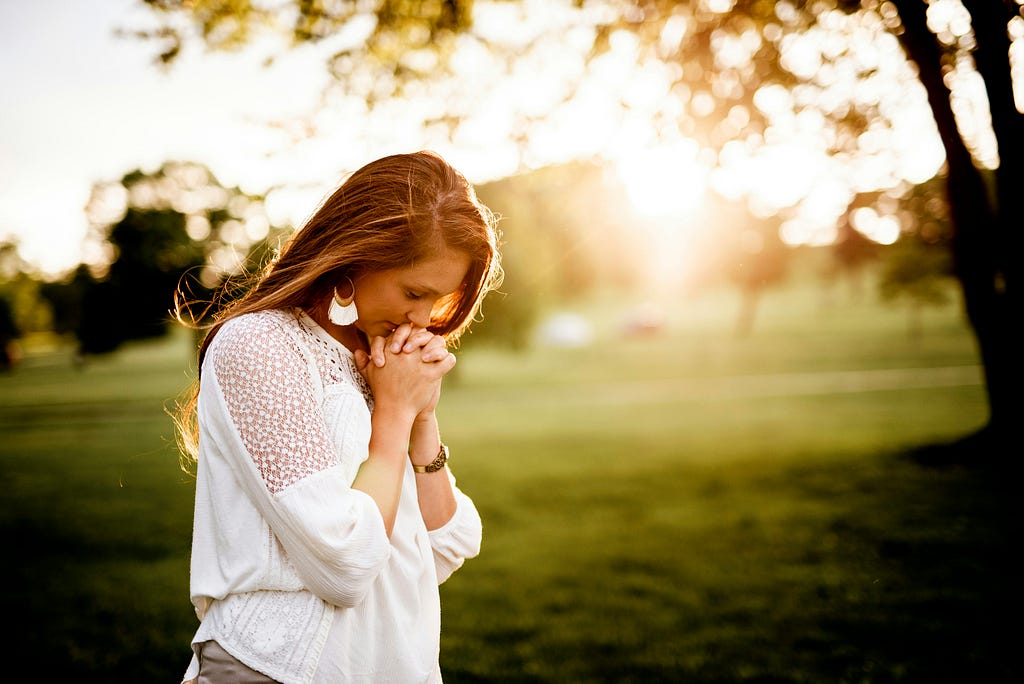 Woman in a field with the light of a sunset shining on her as she prays