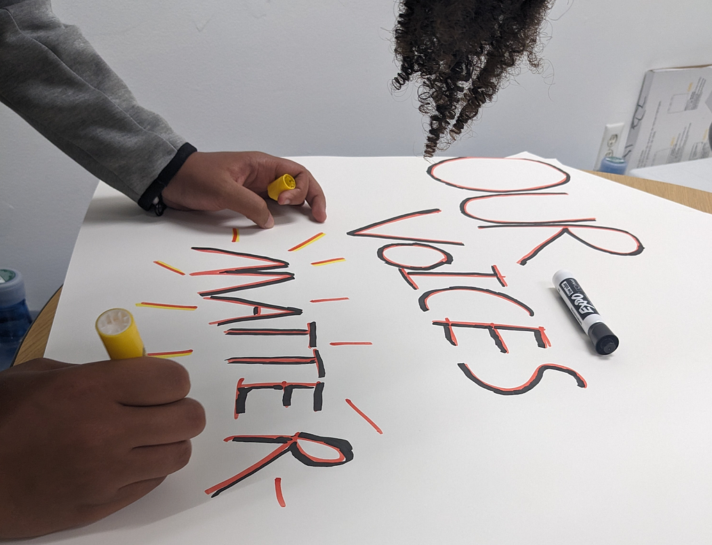 Photo of a student making a sign: “OUR VOICES MATTER”