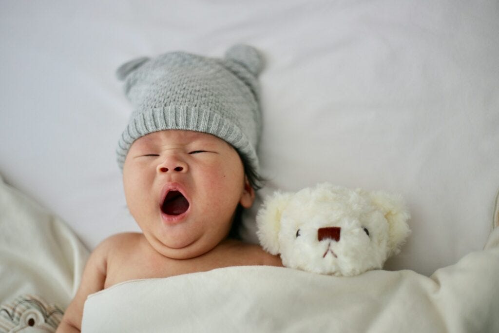 baby's gray knit hat yawning with a white teddy bear.