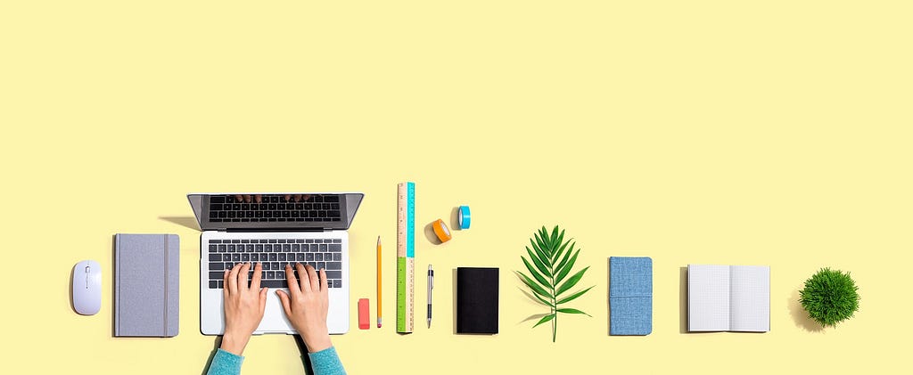 A table top showing a number of items such as notebook, laptop, pen, pencil, etc…