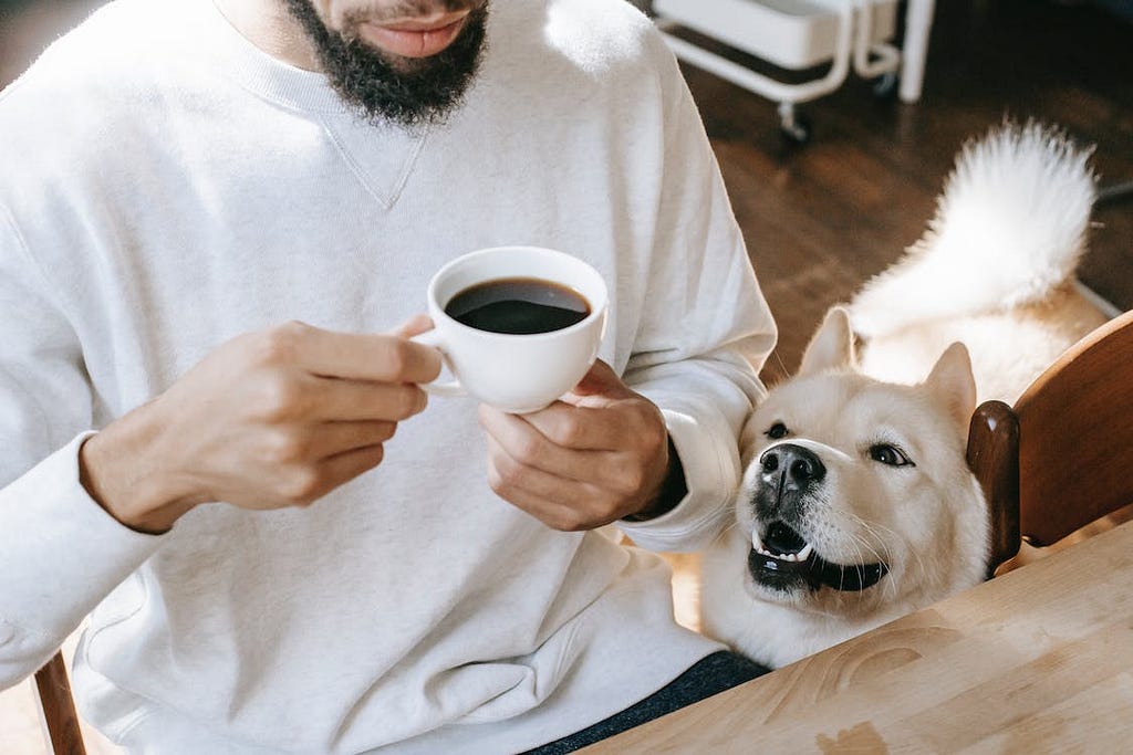 man having black coffee and his dog sitting by him