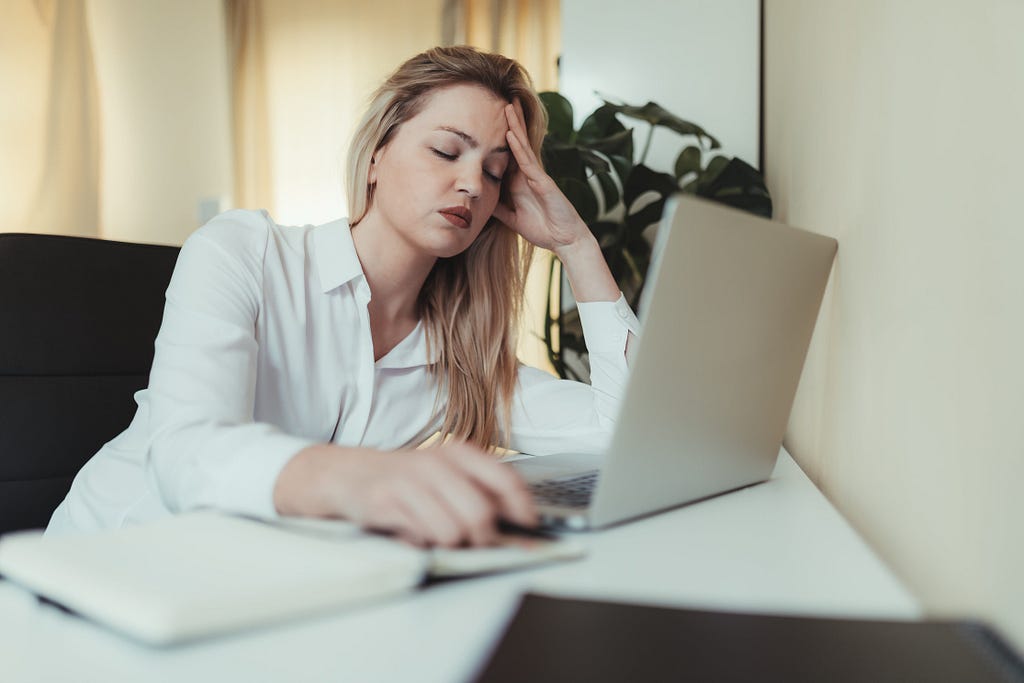 Frustrated woman holding her head with left hand in front of laptop