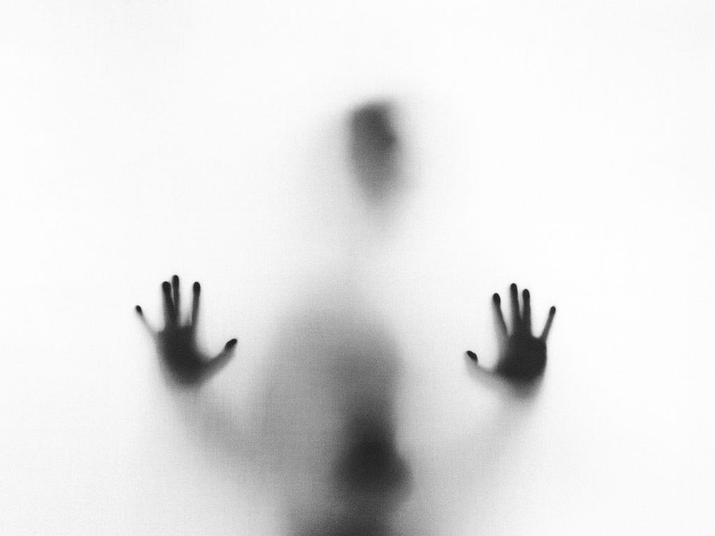 Shadowy figure pressed against frosted glass, only handprints, head, and part of body visible in black