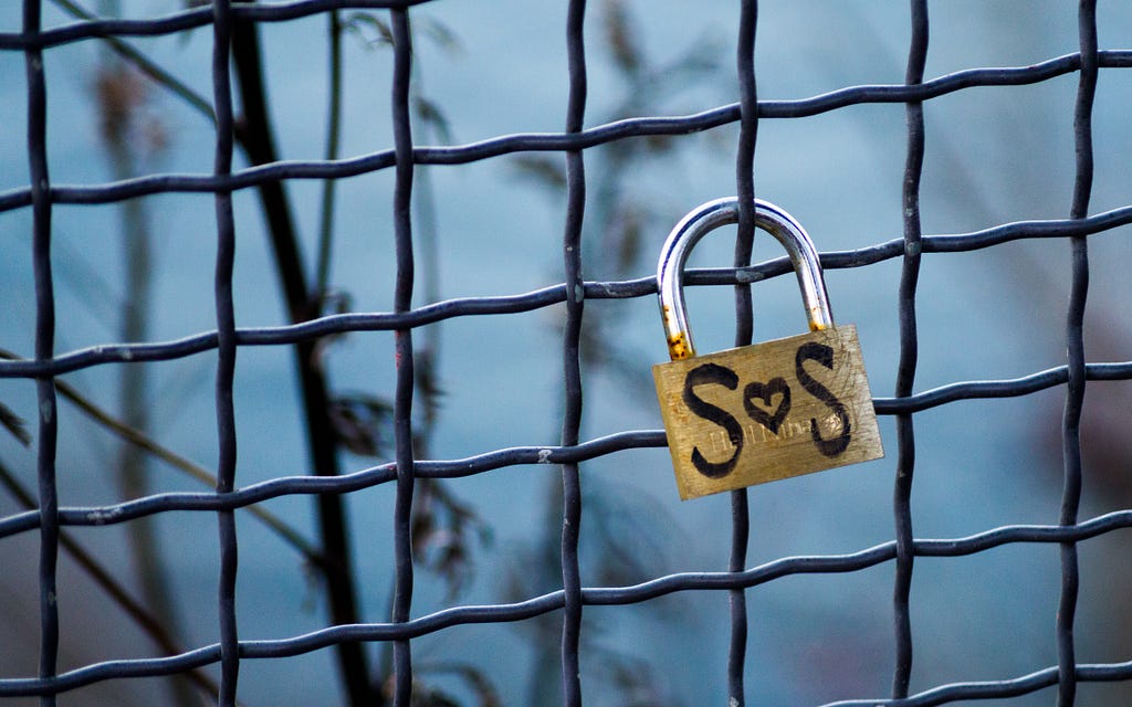 A padlock with the words SOS written on it, attached to a wire grill.